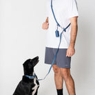 Person holding a blue dog leash with a black dog on a white background